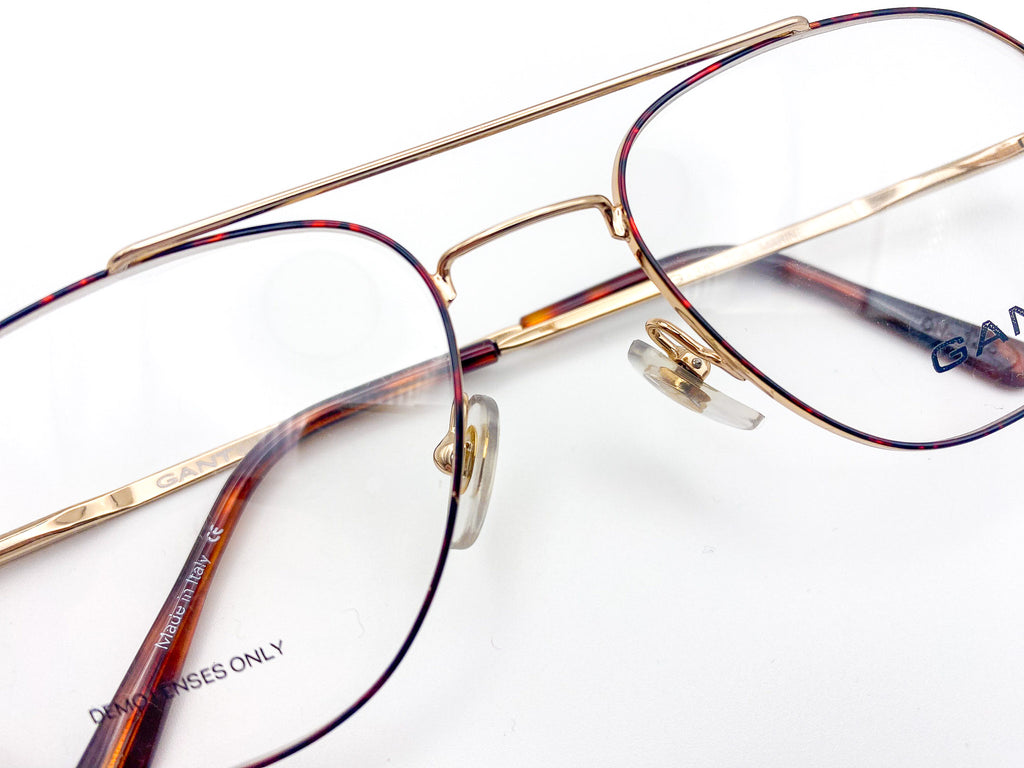 Close-up of a pair of eyeglasses with gold frames and tortoiseshell arms on a white background.