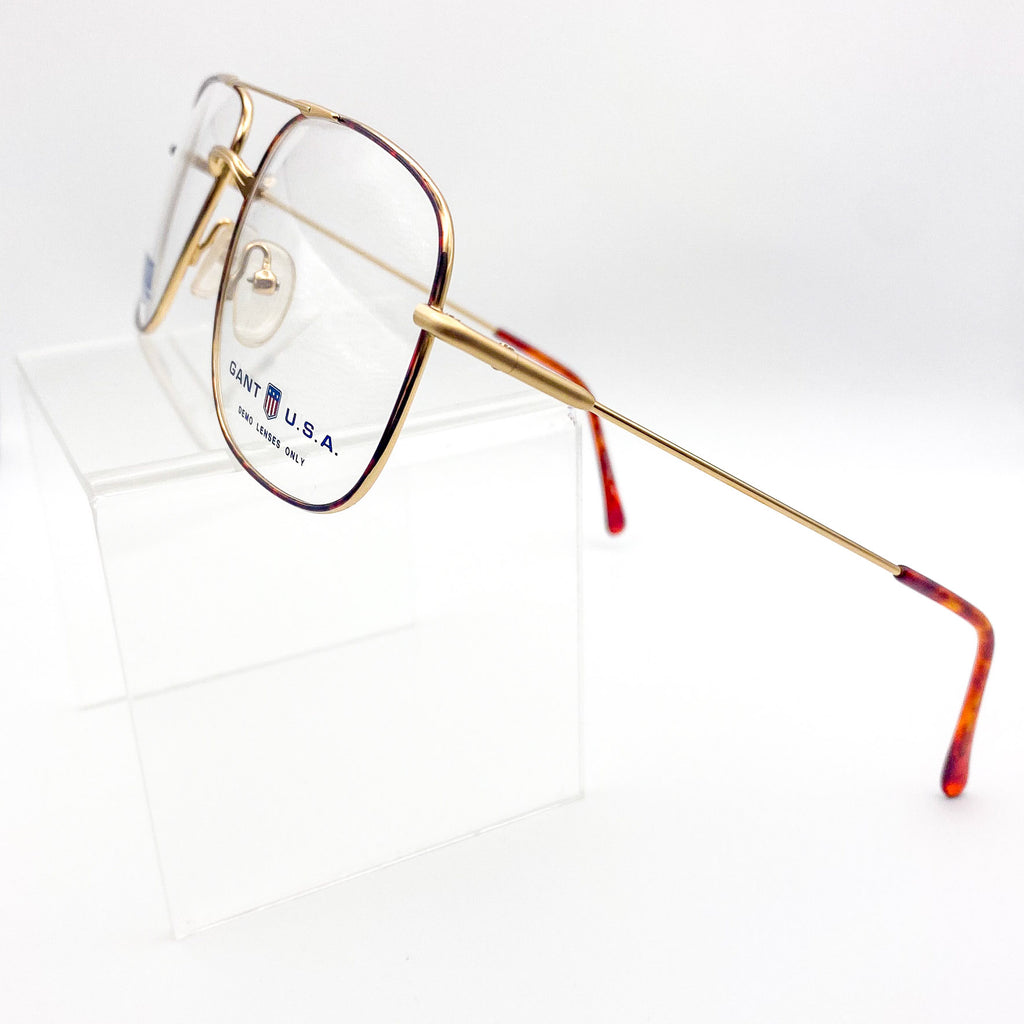 Gold-framed eyeglasses with red-tinted arms on a white background