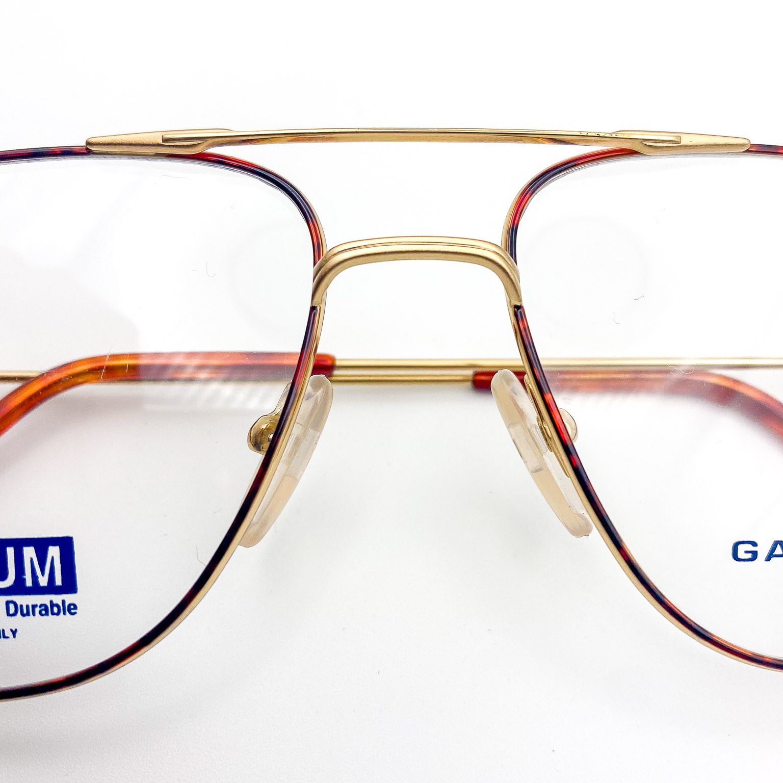 Close-up of a gold-framed aviator eyeglasses with visible brand names on a white background
