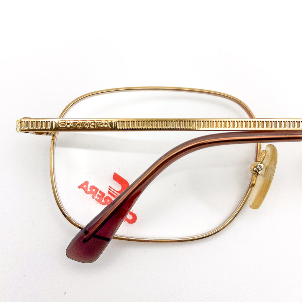 Gold-framed eyeglasses with red logo on lenses on a white background