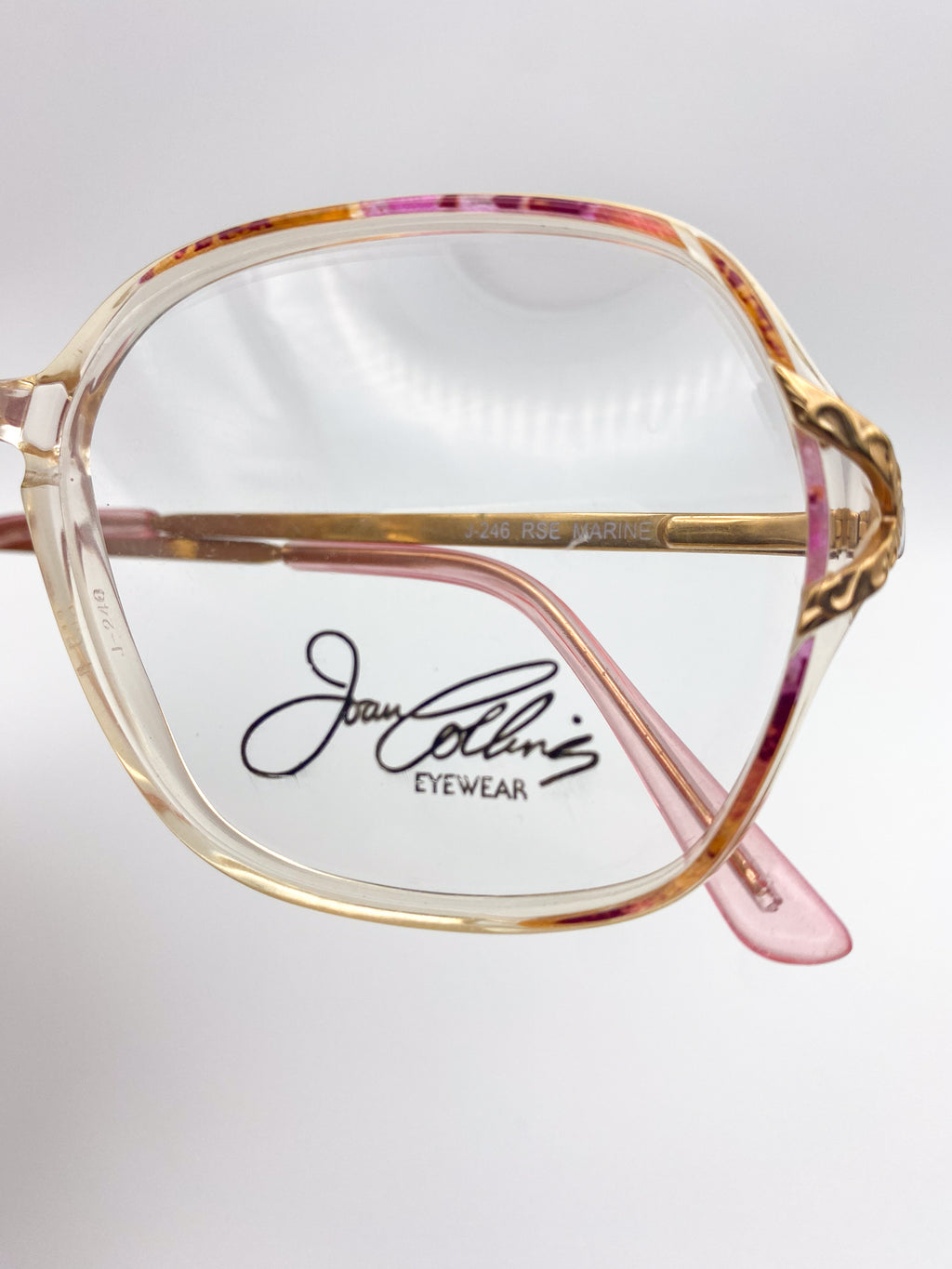 Joan Collins Eyewear glasses with a gold and pink frame on a white background