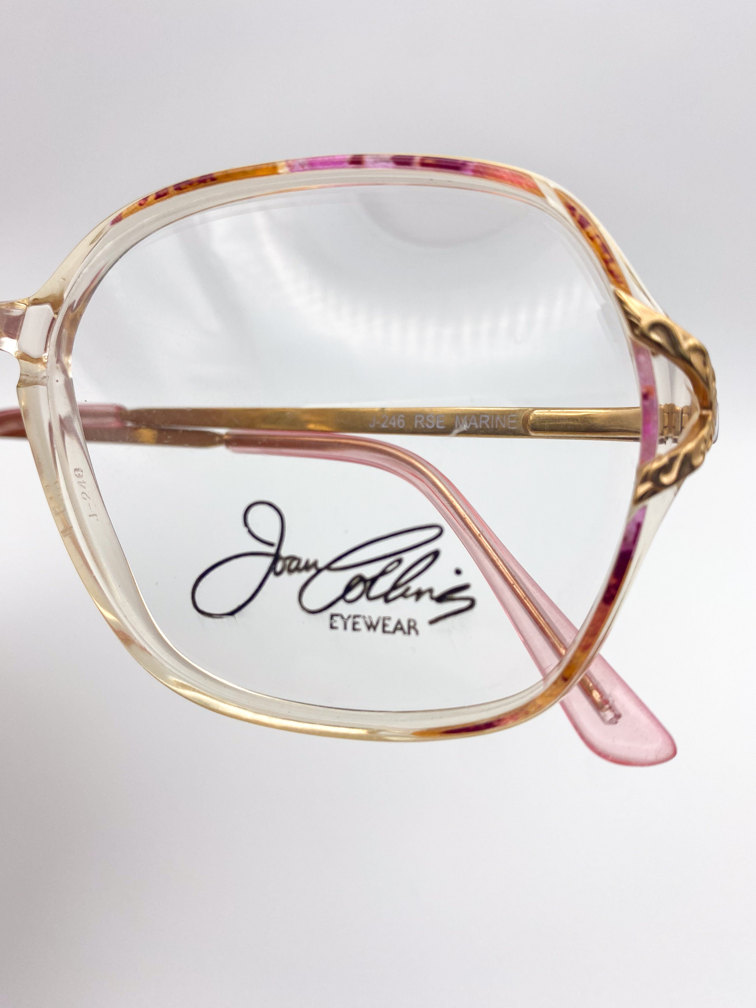 Joan Collins Eyewear glasses with a gold and pink frame on a white background