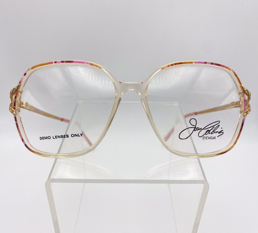 Gold-framed eyeglasses with 'Joan Collins Eyewear' branding on a white background