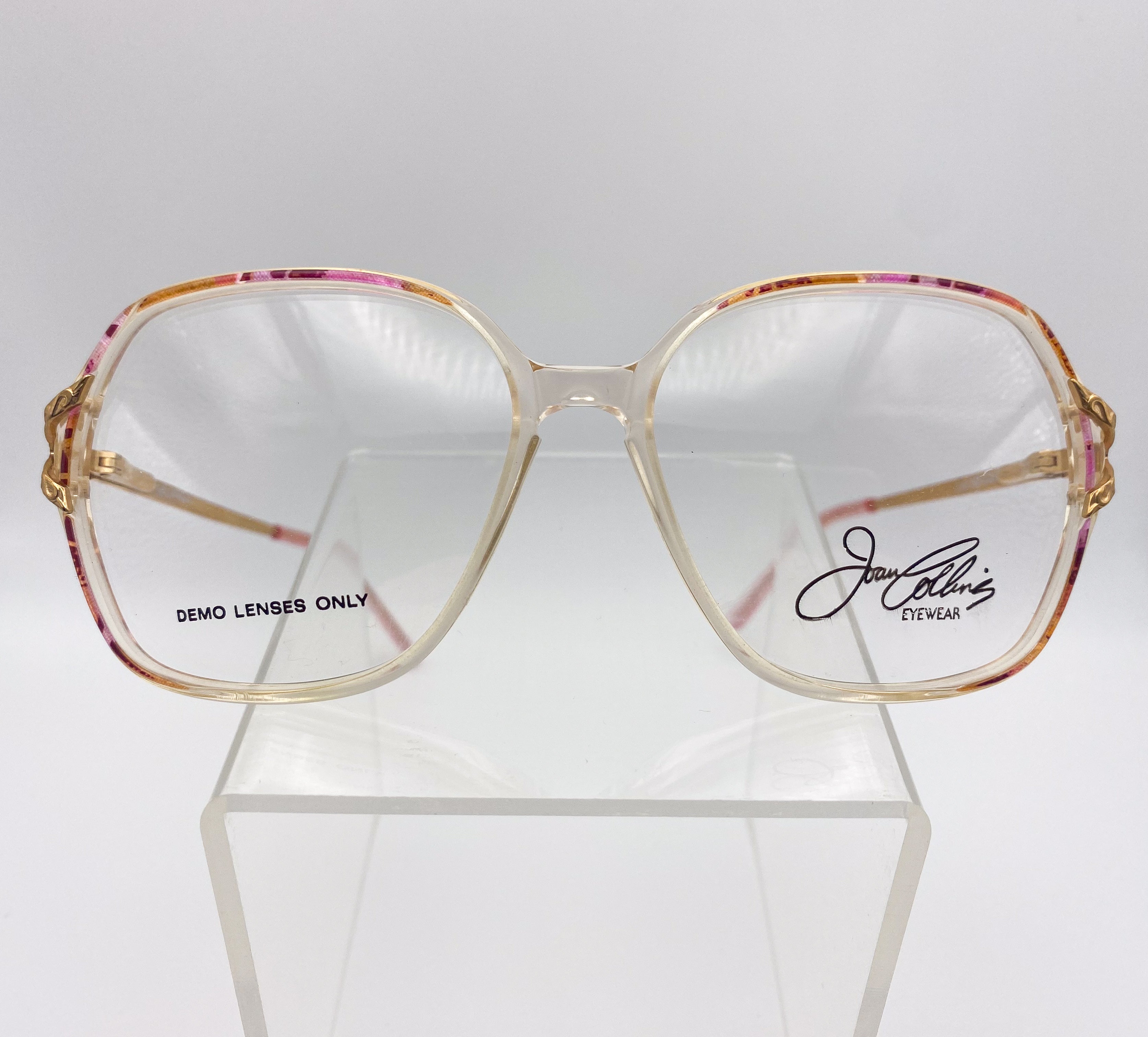 Gold-framed eyeglasses with 'Joan Collins Eyewear' branding on a white background