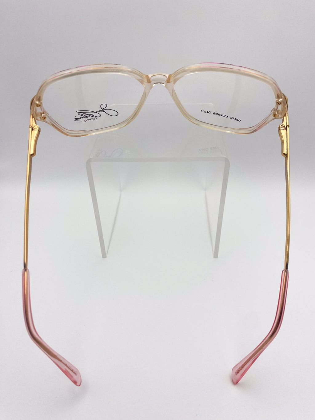 Oversized gold and pink eyeglasses on a clear stand against a white background