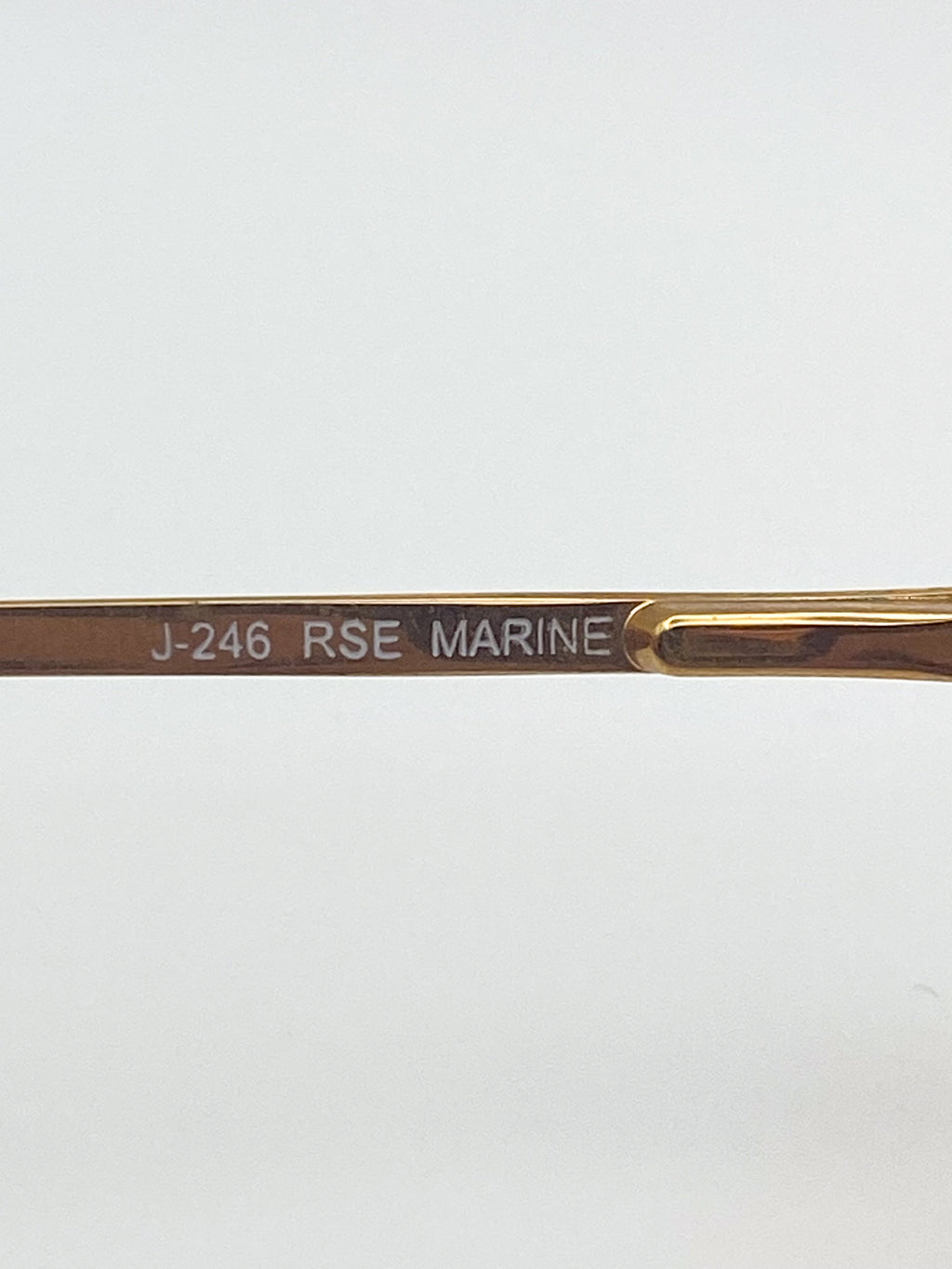 Gold glasses arm with 'J-246 RSE MARINE' engraving on a white background
