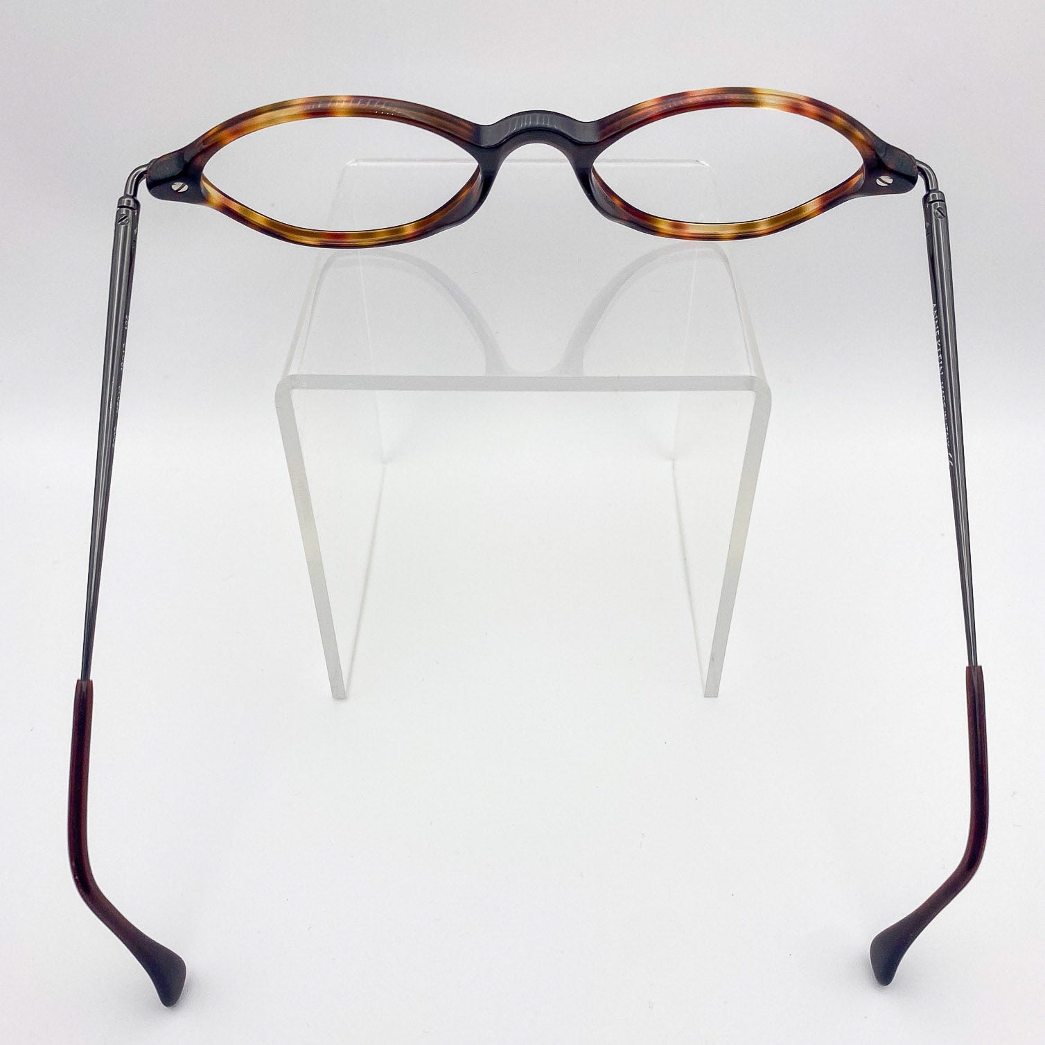 Eyeglasses with tortoiseshell frame on a clear stand against a white background