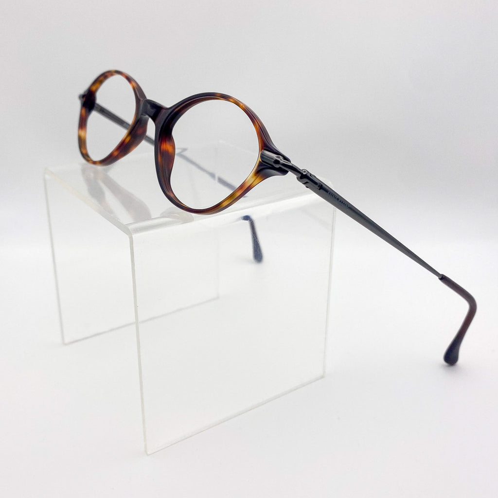 Oval eyeglasses with tortoiseshell frame on a clear stand against a light gray background