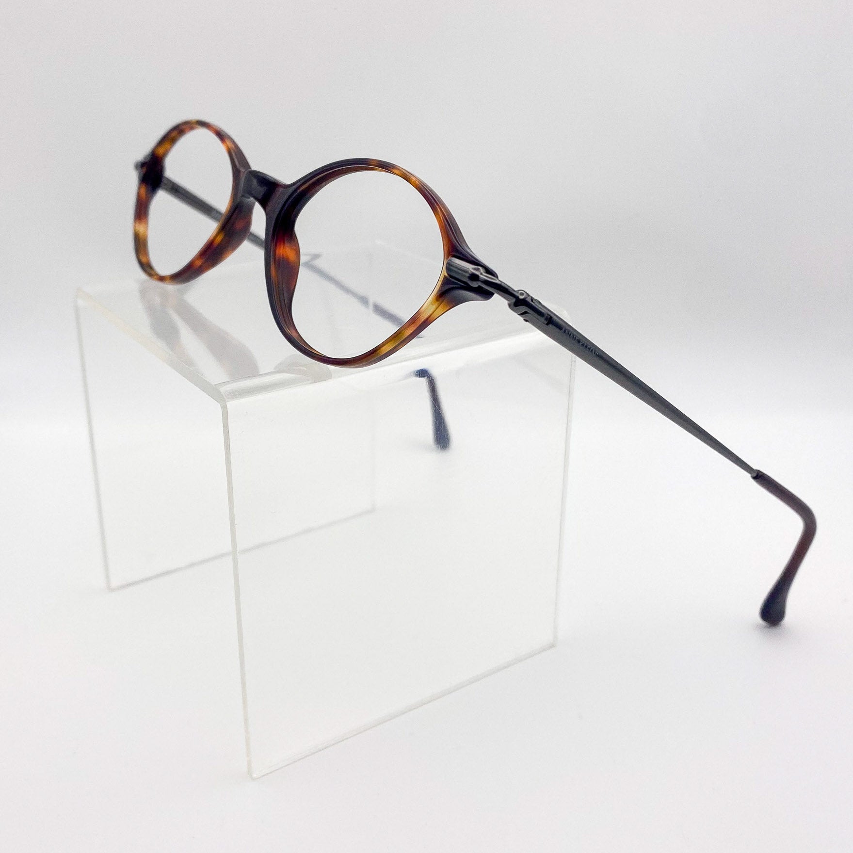 Oval eyeglasses with tortoiseshell frame on a clear stand against a light gray background