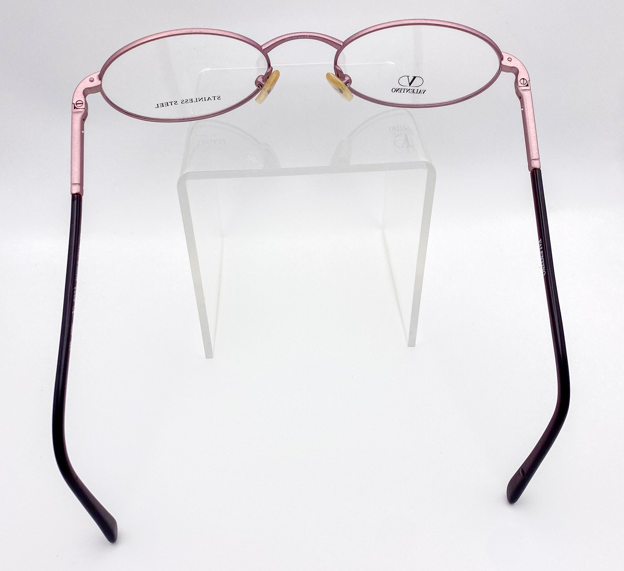 Metallic lavender oval eyeglasses on a clear stand against a white background