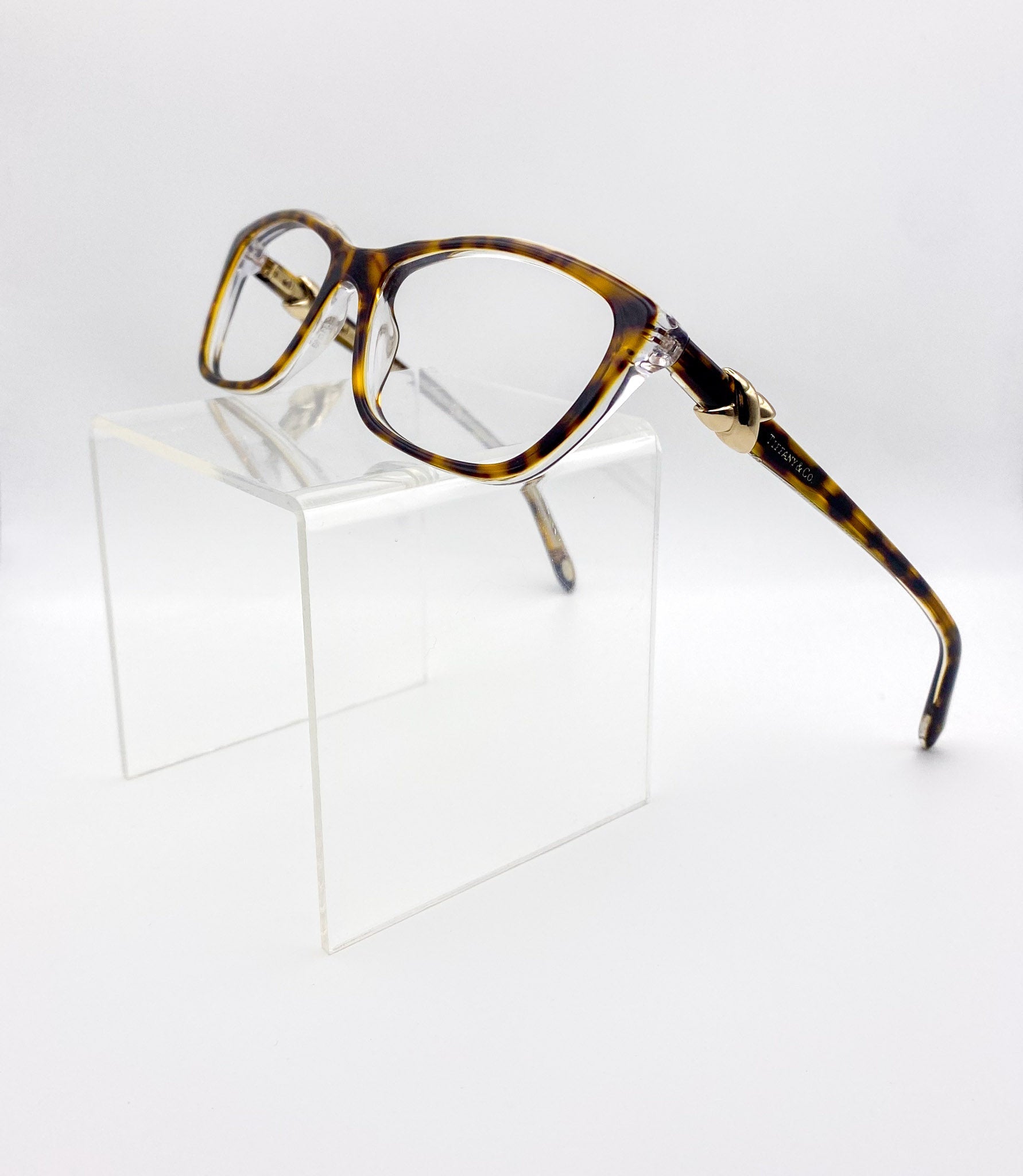 Tortoiseshell eyeglasses on a clear stand against a white background