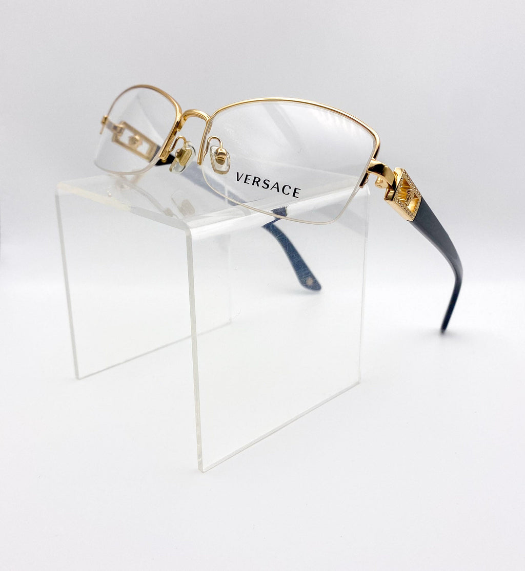 Versace eyeglasses with gold frame and black accents on a clear stand against a white background
