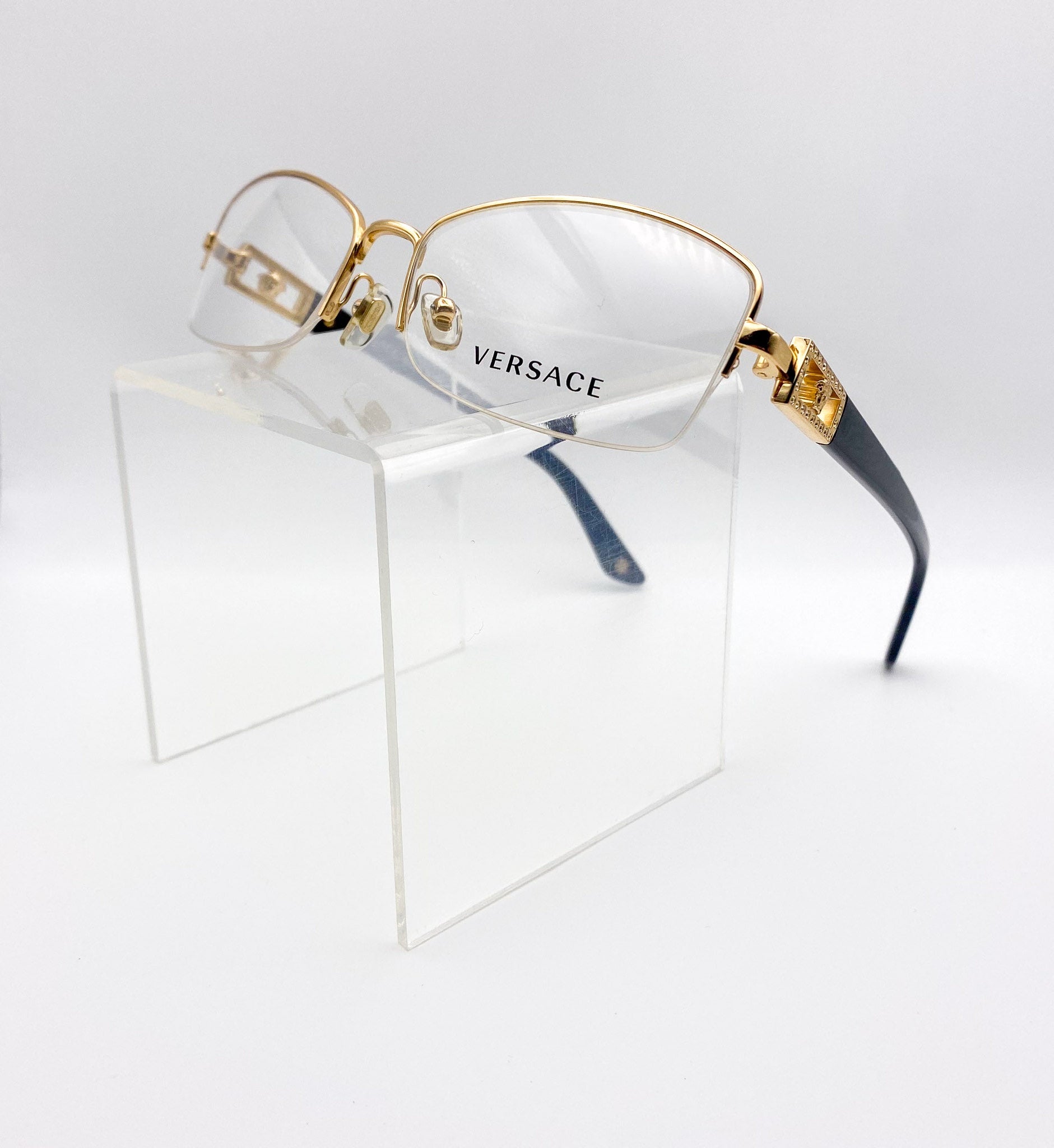 Versace eyeglasses with gold frame and black accents on a clear stand against a white background