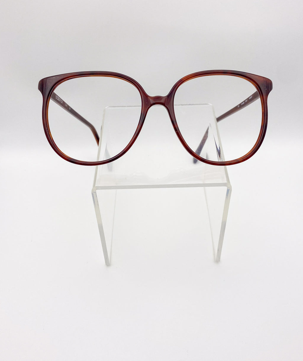 Vintage oversized eyeglasses on a clear stand against a white background