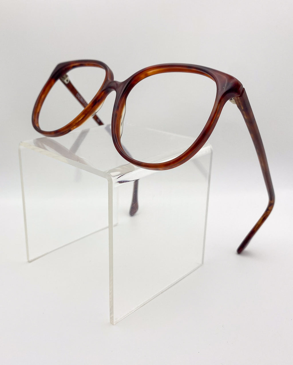 Tortoiseshell eyeglasses on a clear stand against a white background