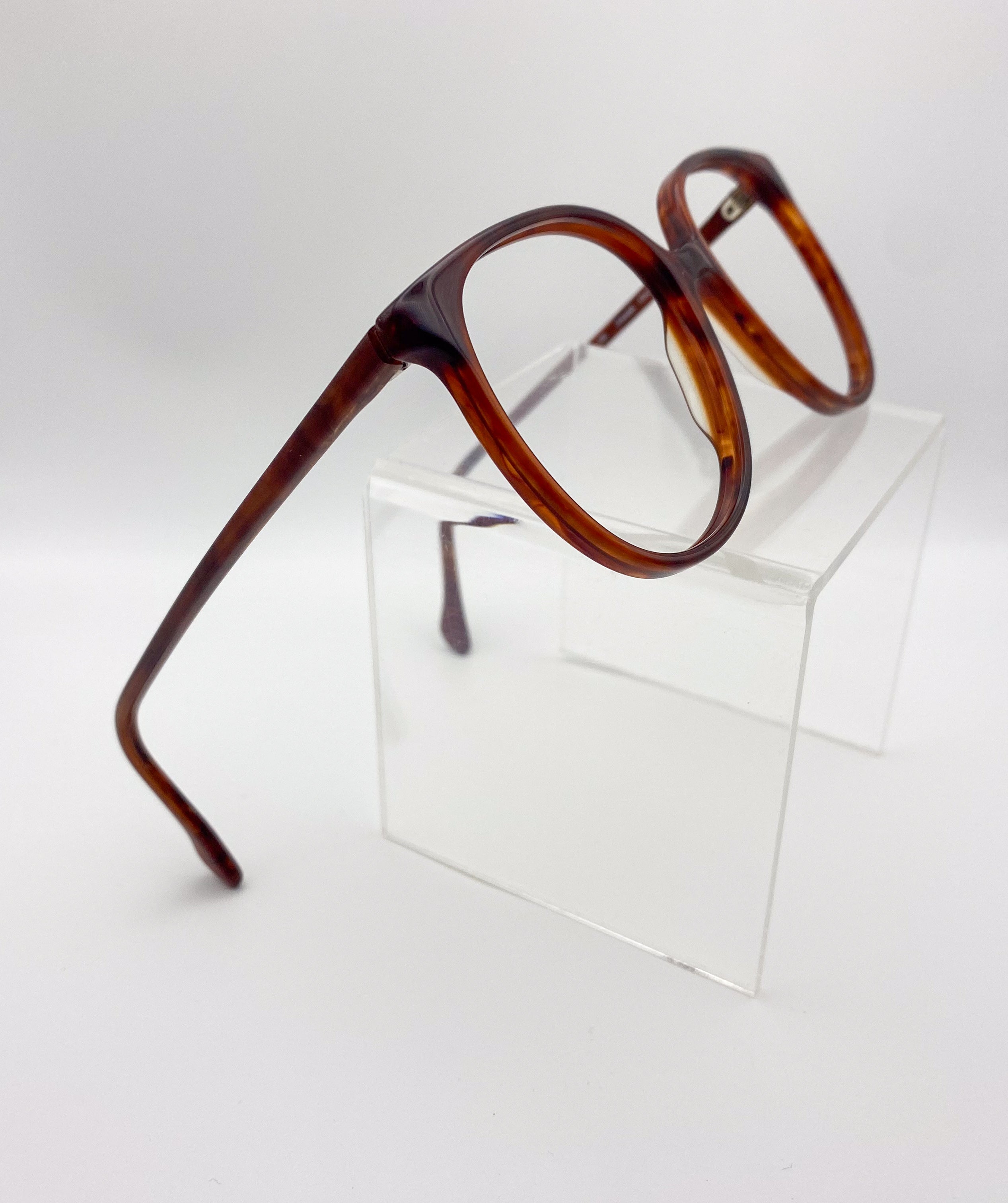 Tortoiseshell eyeglasses on a clear stand against a white background