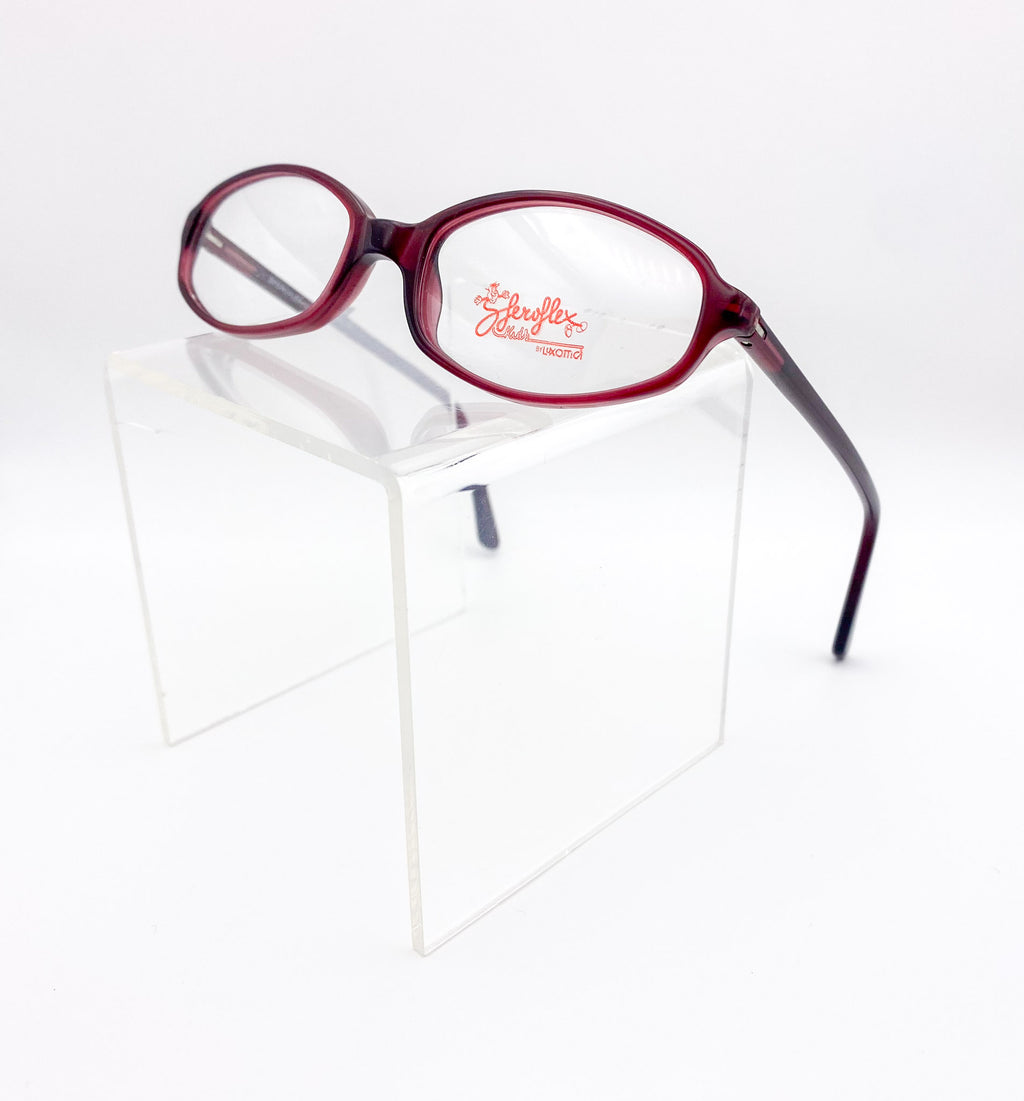 Red eyeglasses on a clear stand with 'Sferoflex' branding.
