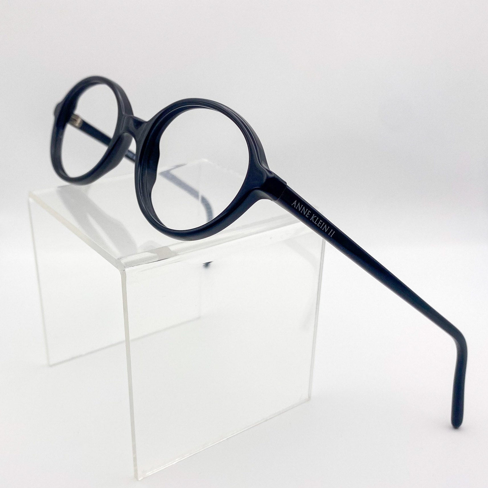 1990s black eyeglasses on a clear acrylic stand against a white background