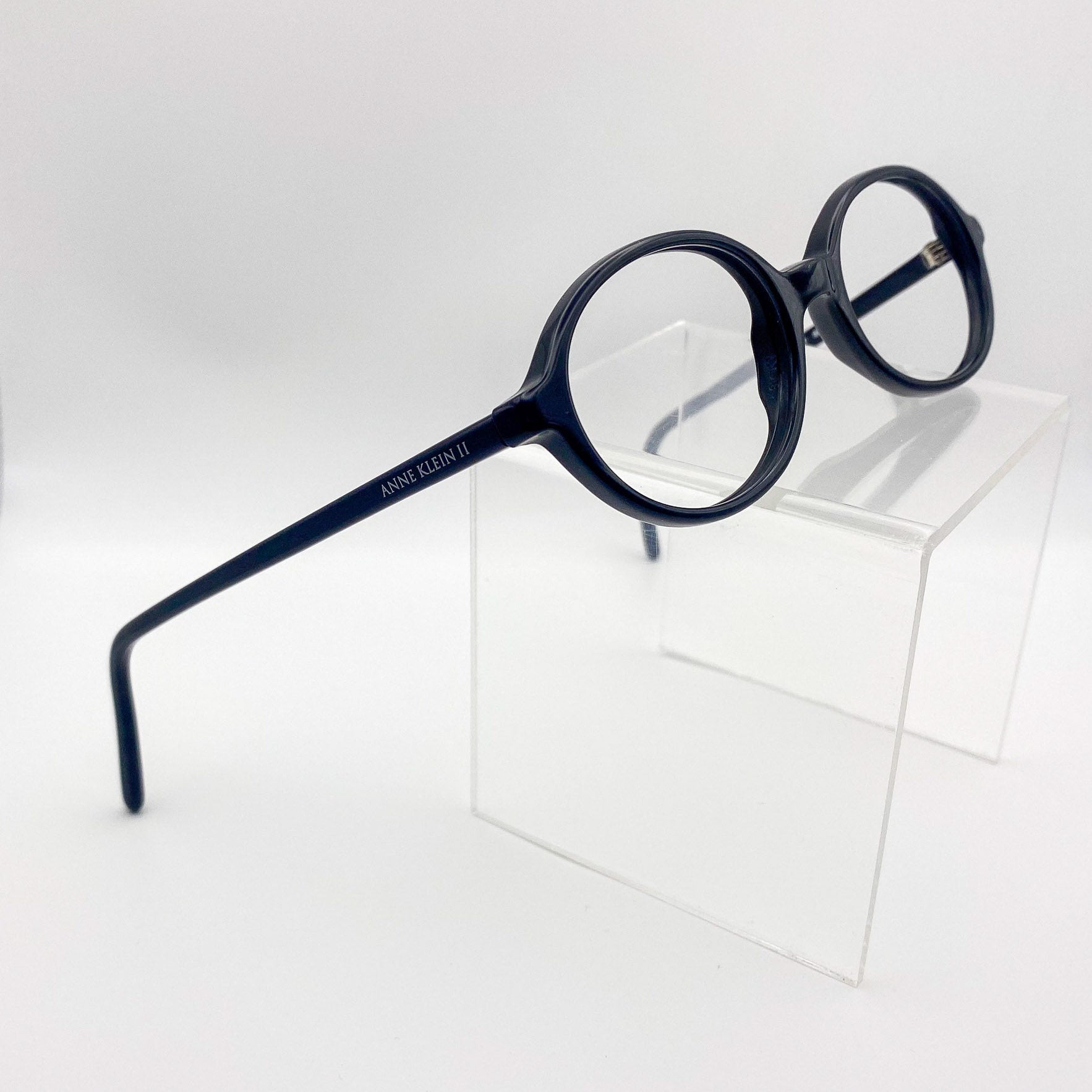Round black eyeglasses on a clear stand against a white background