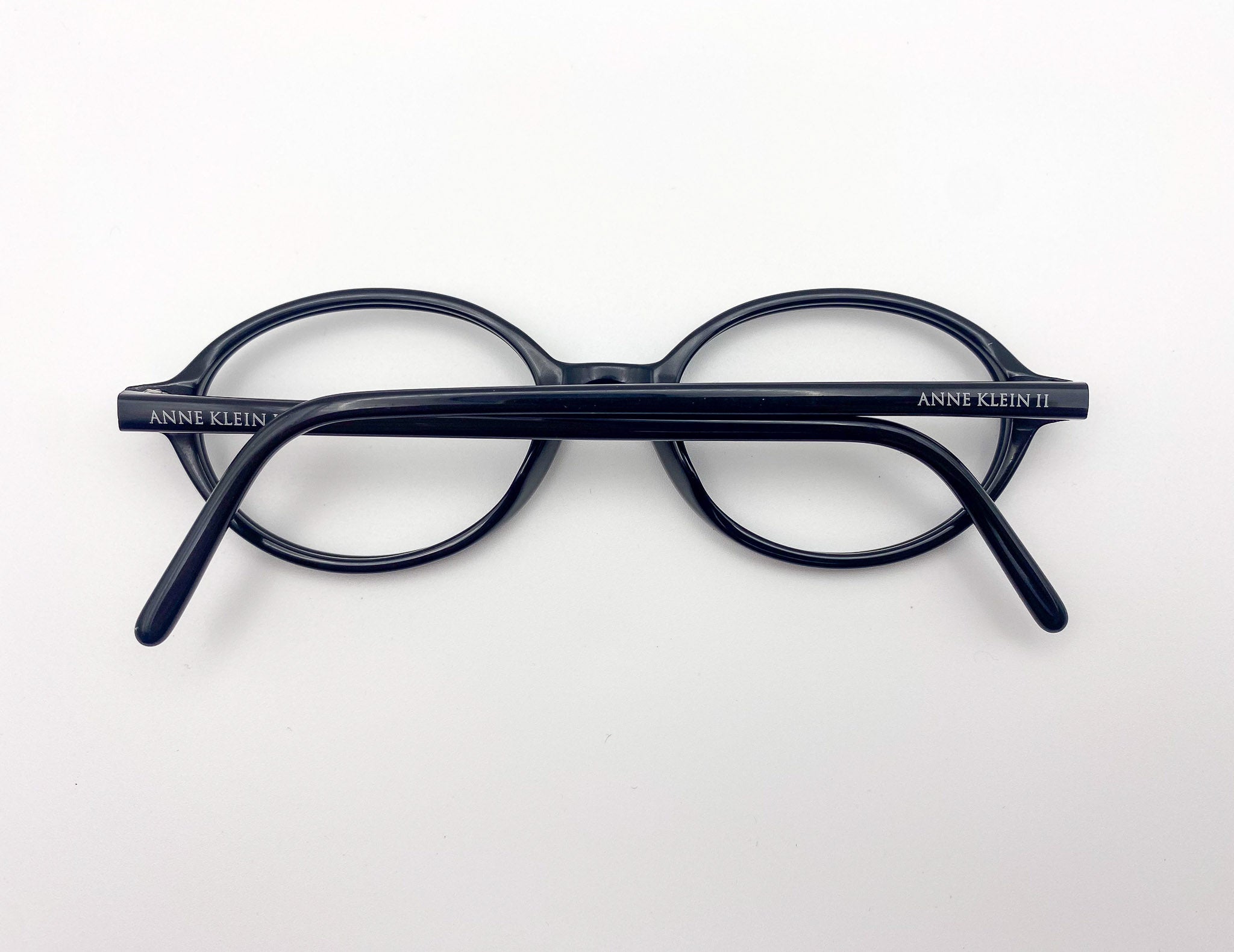 Black eyeglasses with 'Anne Klein' branding on a white background