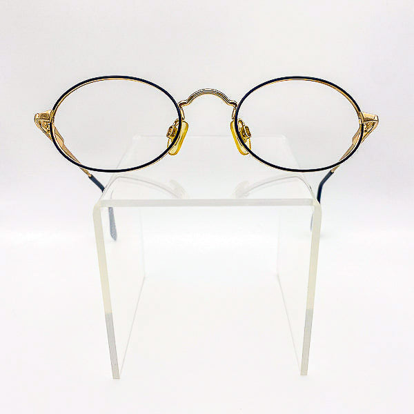 Oval-round eyeglasses with gold frames on a clear stand against a white background