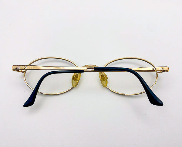 Gold-framed eyeglasses with black temple tips on a light gray background