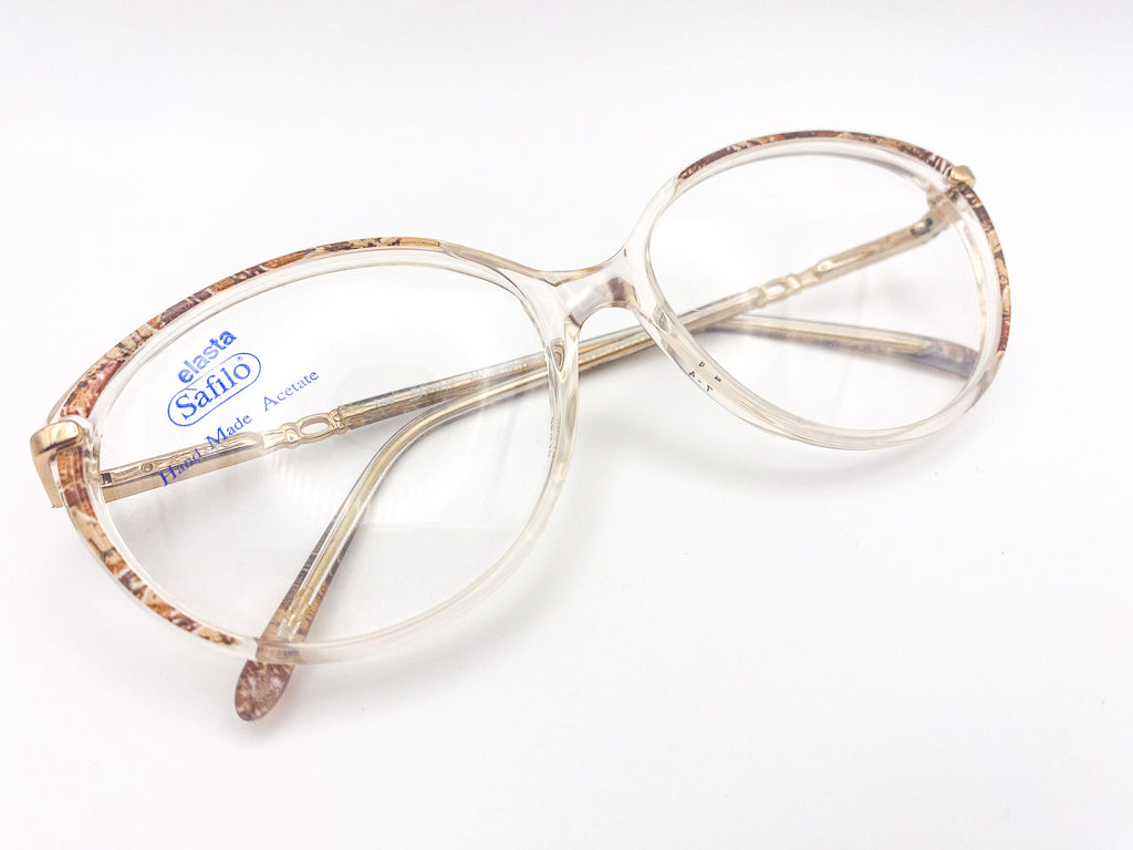 Vintage eyeglasses with a clear frame and tortoise detail on a white background
