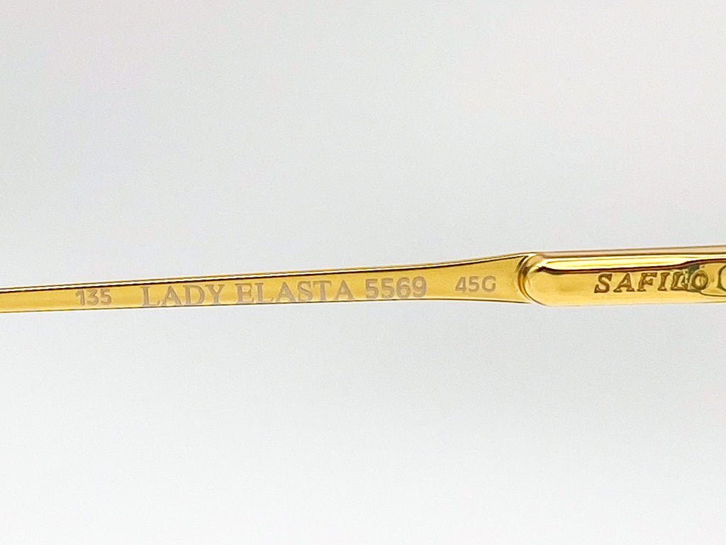 Gold eyeglasses with brand name on a light gray background