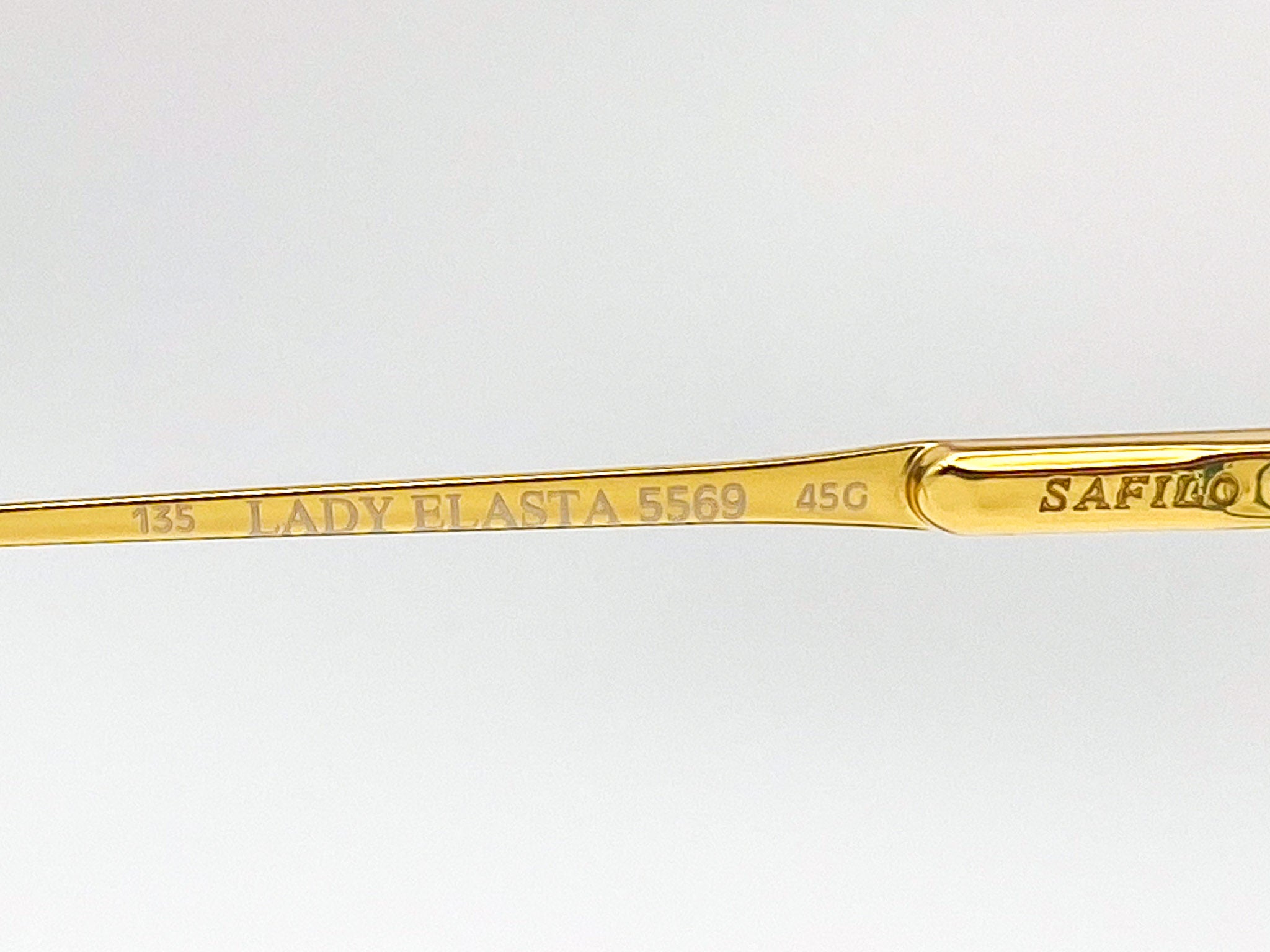 Gold eyeglasses with brand name on a light gray background