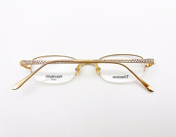 Gold-framed semi-rim glasses with 'Vera Wang' branding on a white background