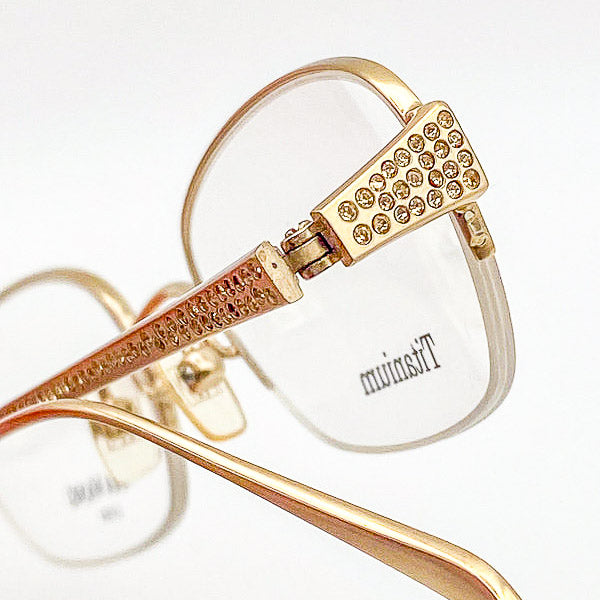 Gold-framed eyeglasses with 'Titanium' branding on a white background