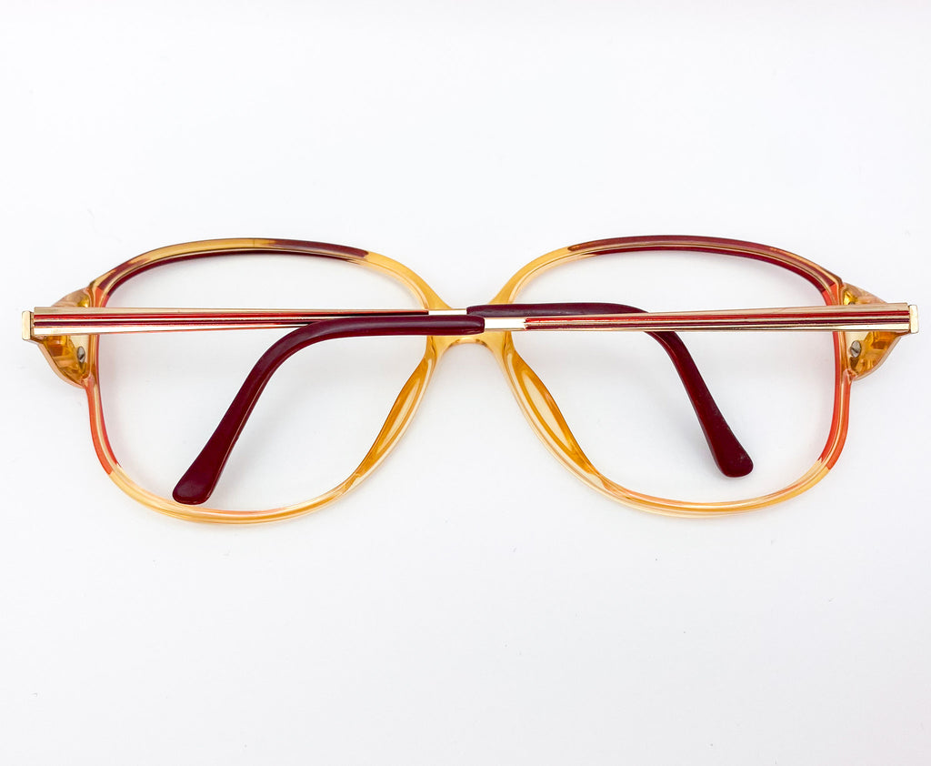 Vintage-style eyeglasses with a gold and red frame on a white background