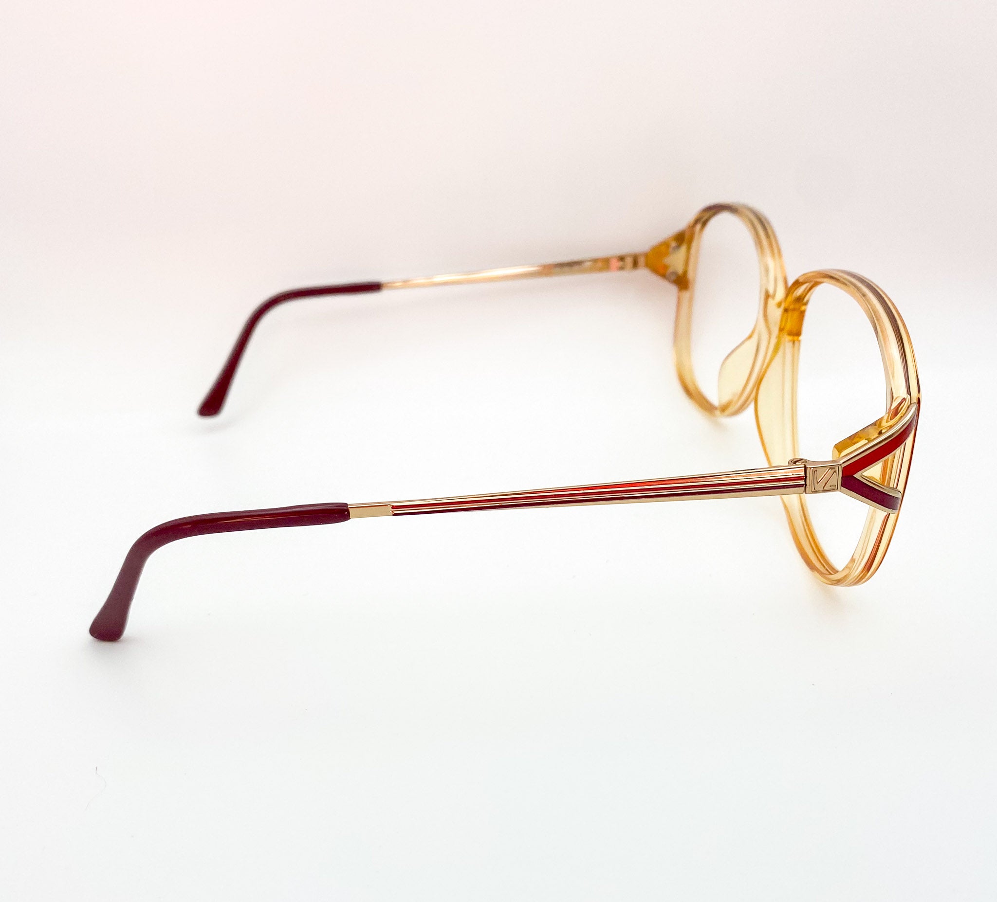 Pair of eyeglasses with gold frame and red-brown arms on a white background