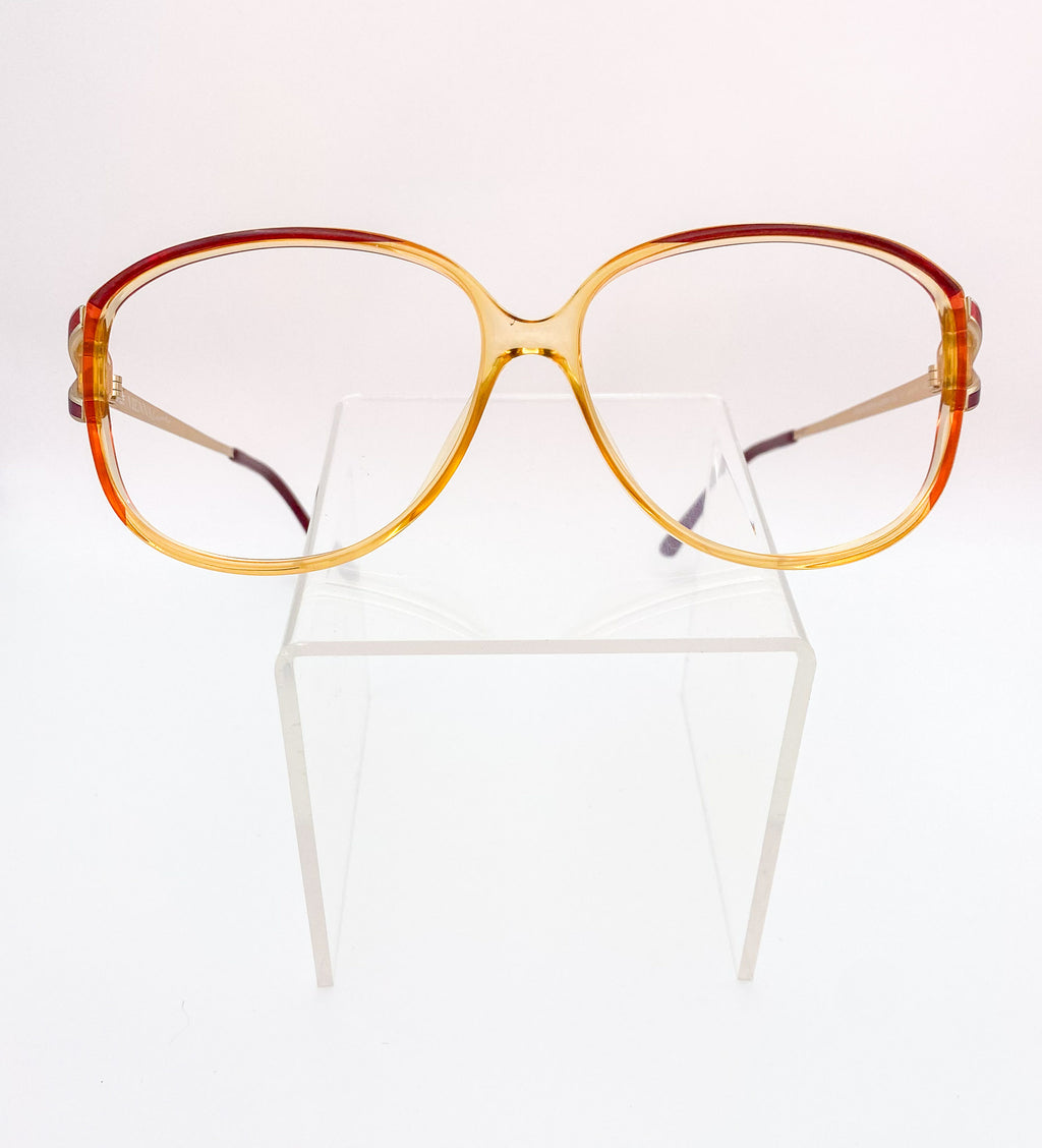 Vintage-style eyeglasses with a tortoiseshell frame on a clear stand against a white background