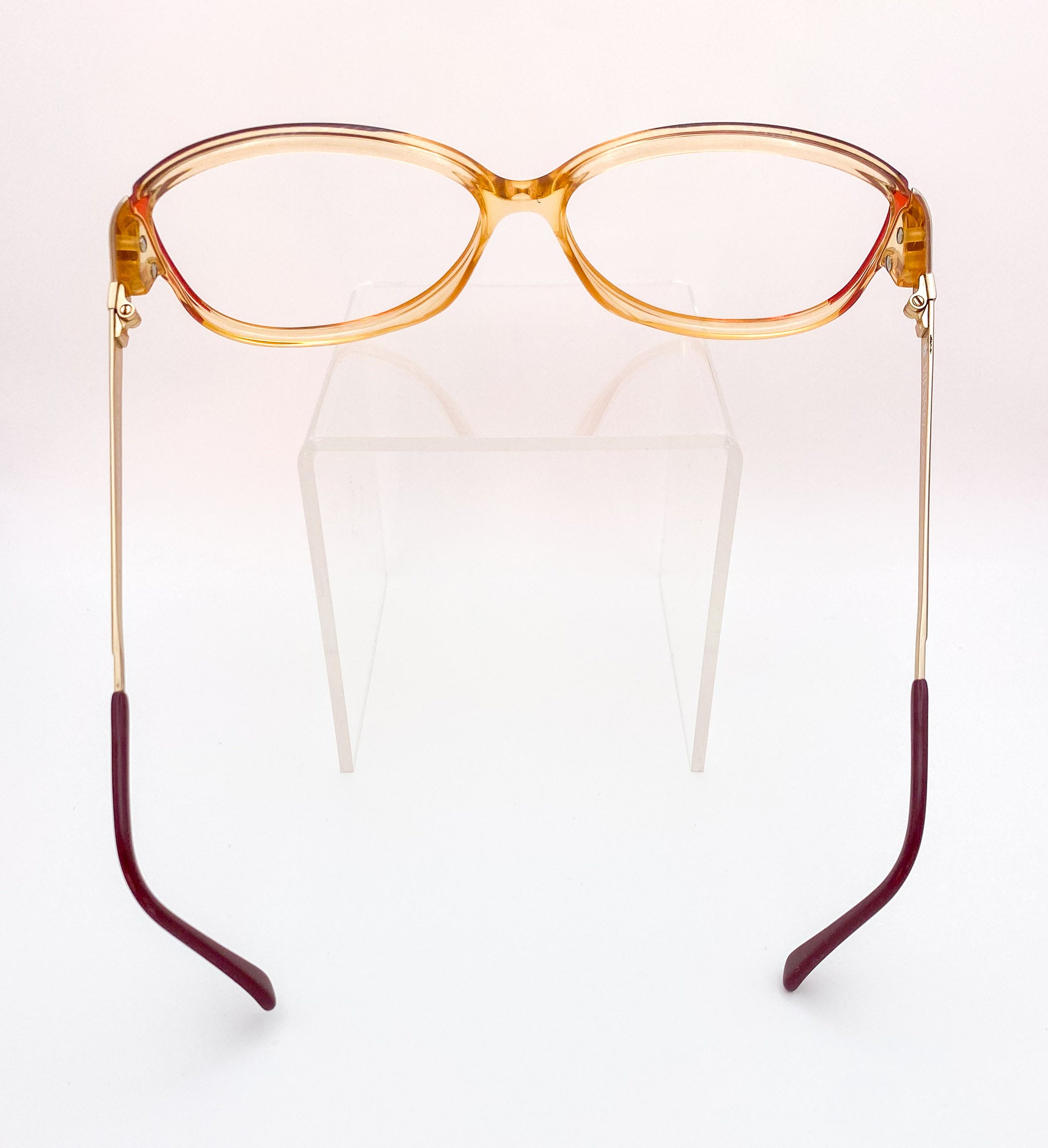 Eyeglasses with a transparent orange frame and burgundy arms on a white background
