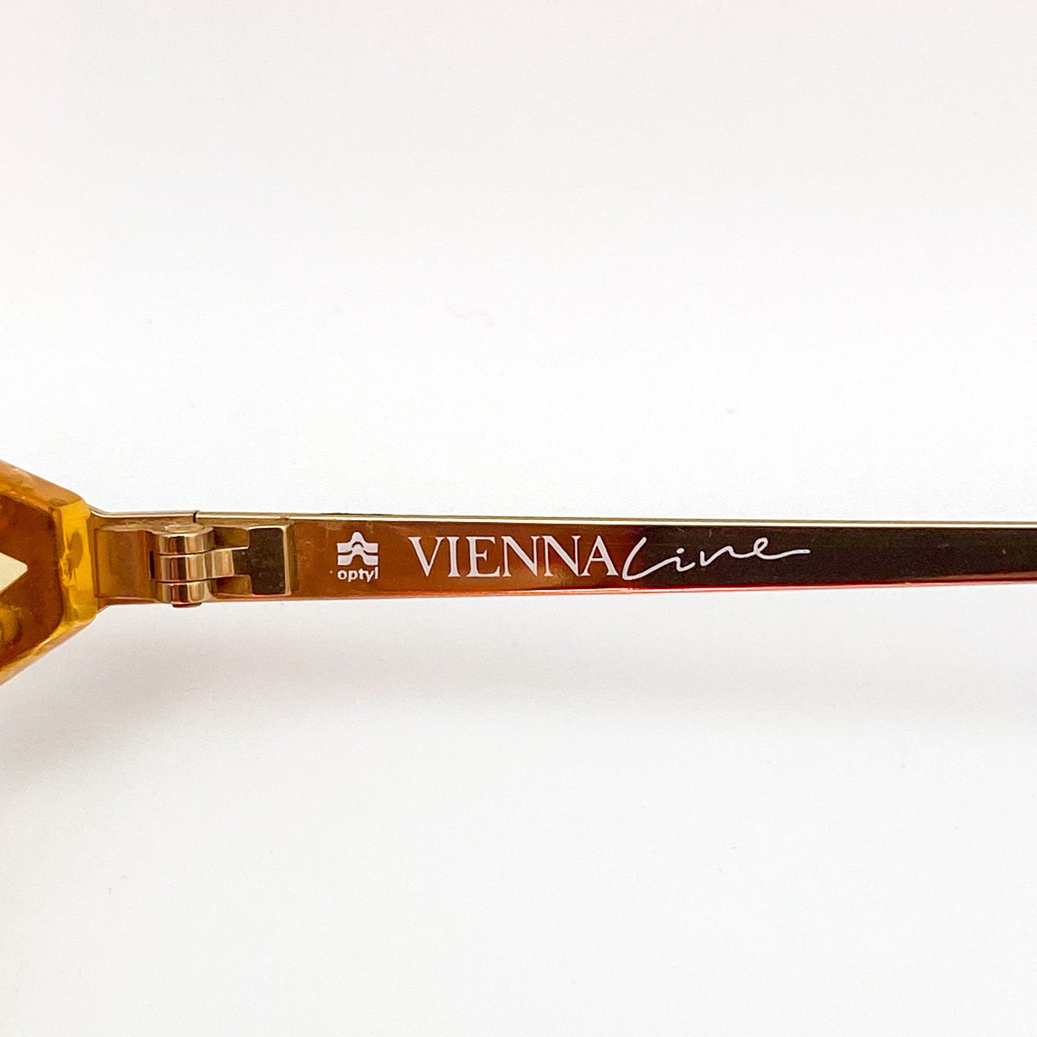 Close-up of a gold-framed eyeglasses with 'VIENNA LINE' branding on a white background