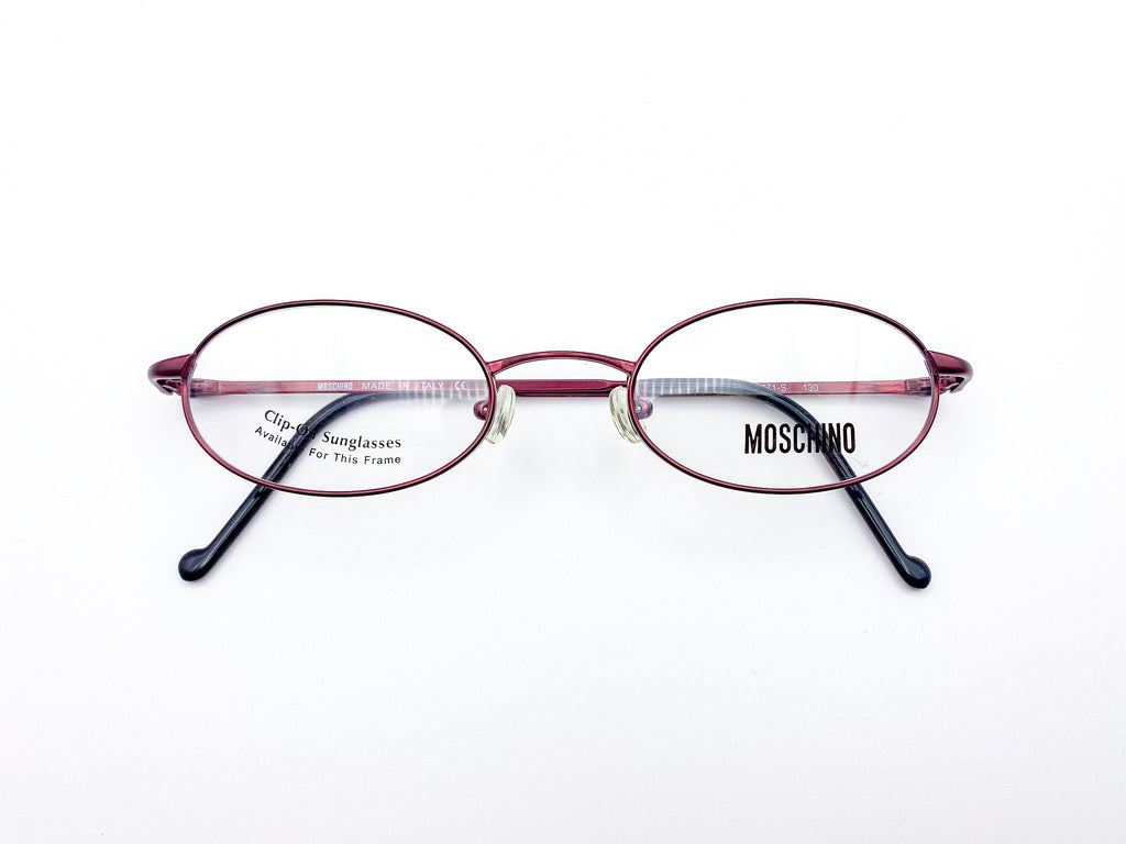 Oval red eyeglasses with black temples on a white background, featuring the Moschino logo.