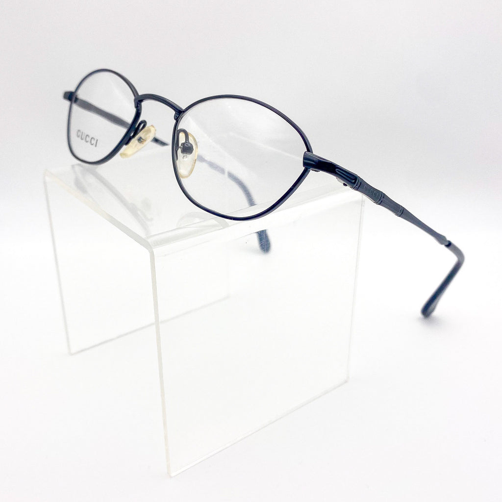 Vintage Gucci eyeglasses on a clear stand with a white background
