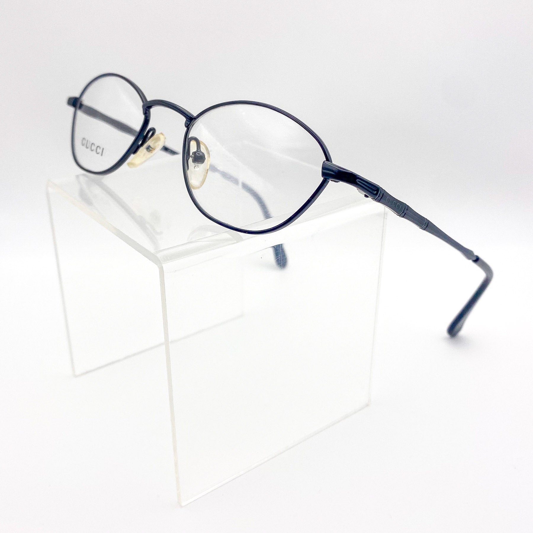 Vintage Gucci eyeglasses on a clear stand with a white background
