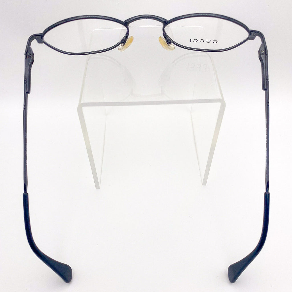 Black eyeglasses on a clear stand with 'GUCCI' branding.