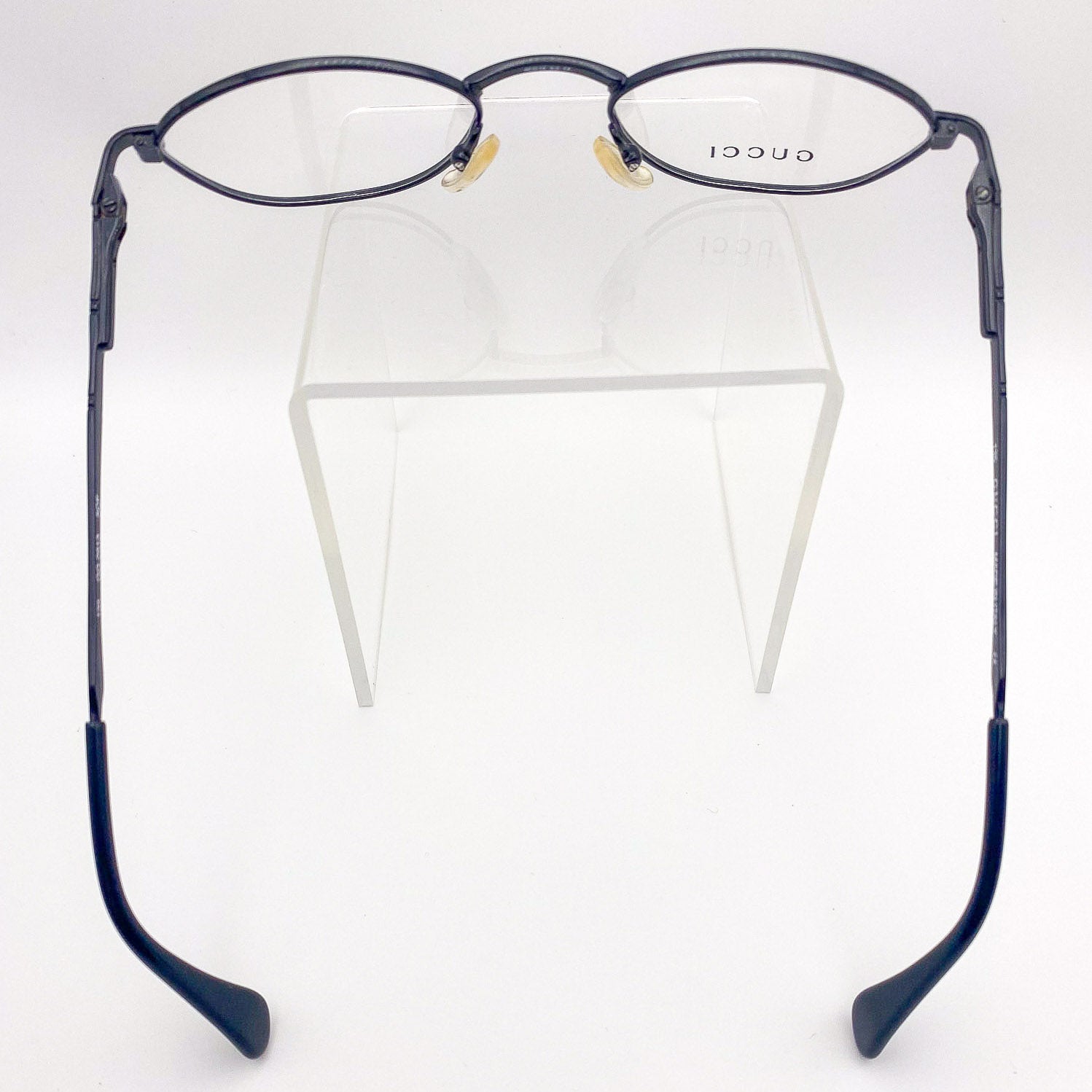 Black eyeglasses on a clear stand with 'GUCCI' branding.