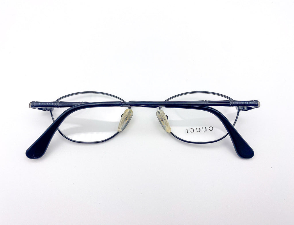 1990s oval pair of eyeglasses with 'Gucci' branding on a white background