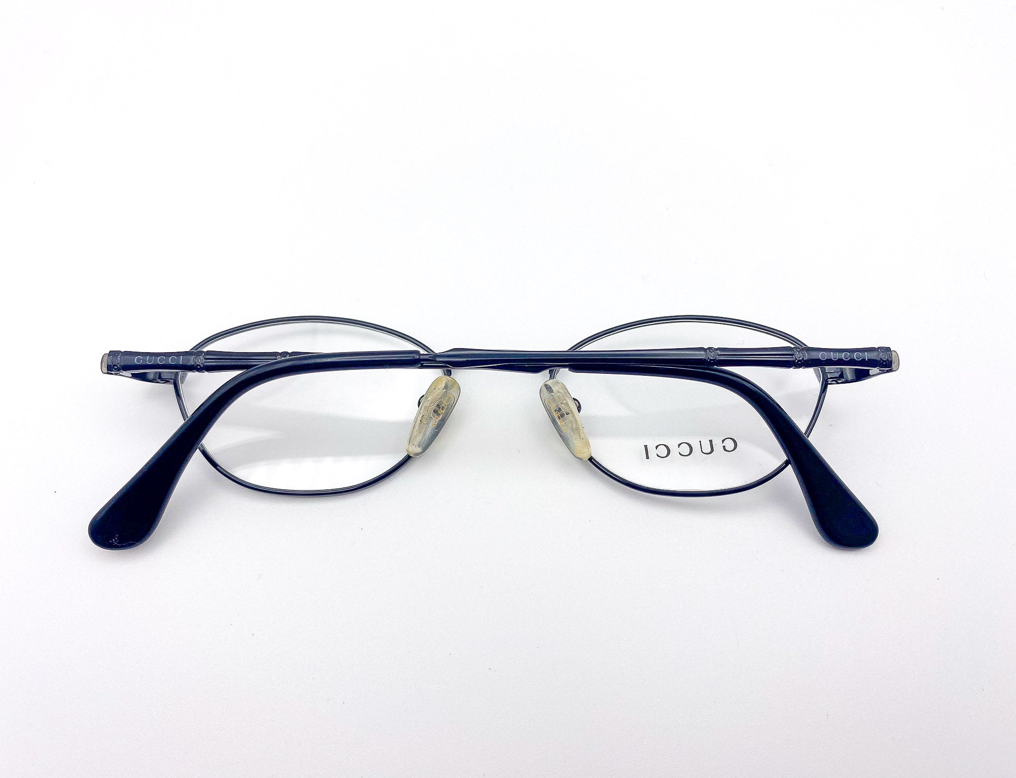 1990s oval pair of eyeglasses with 'Gucci' branding on a white background