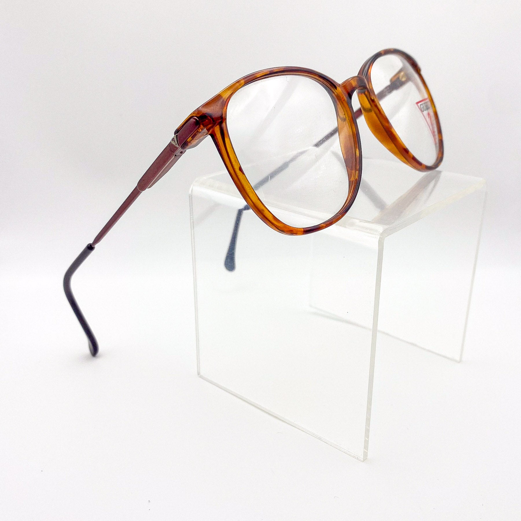 Tortoiseshell eyeglasses on a clear stand against a white background