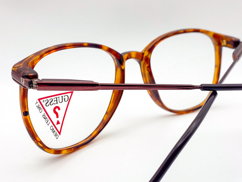 Close-up of tortoiseshell glasses with a visible brand logo on a white background