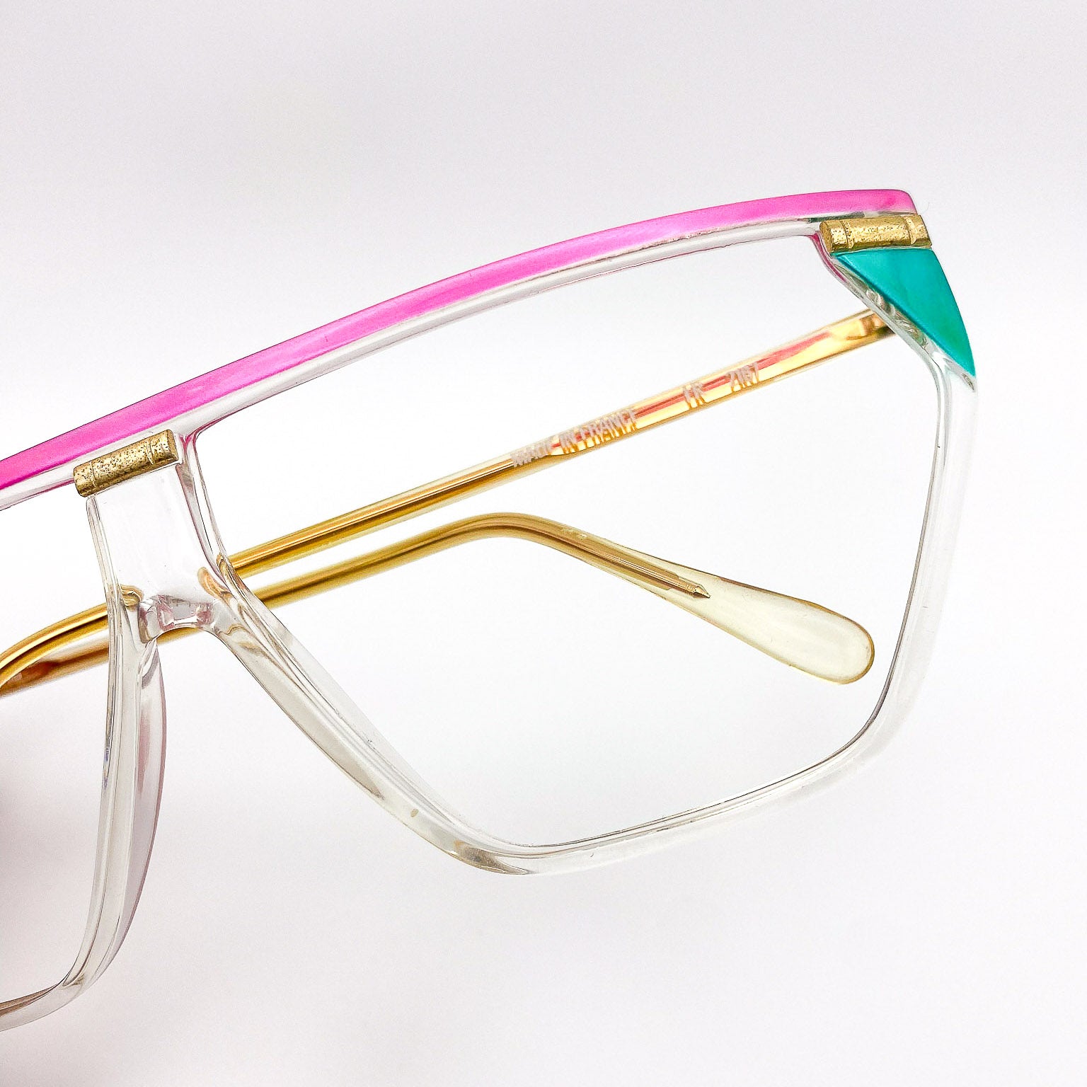 1980s multicolored eyeglasses with pink, gold, and teal on a light gray background