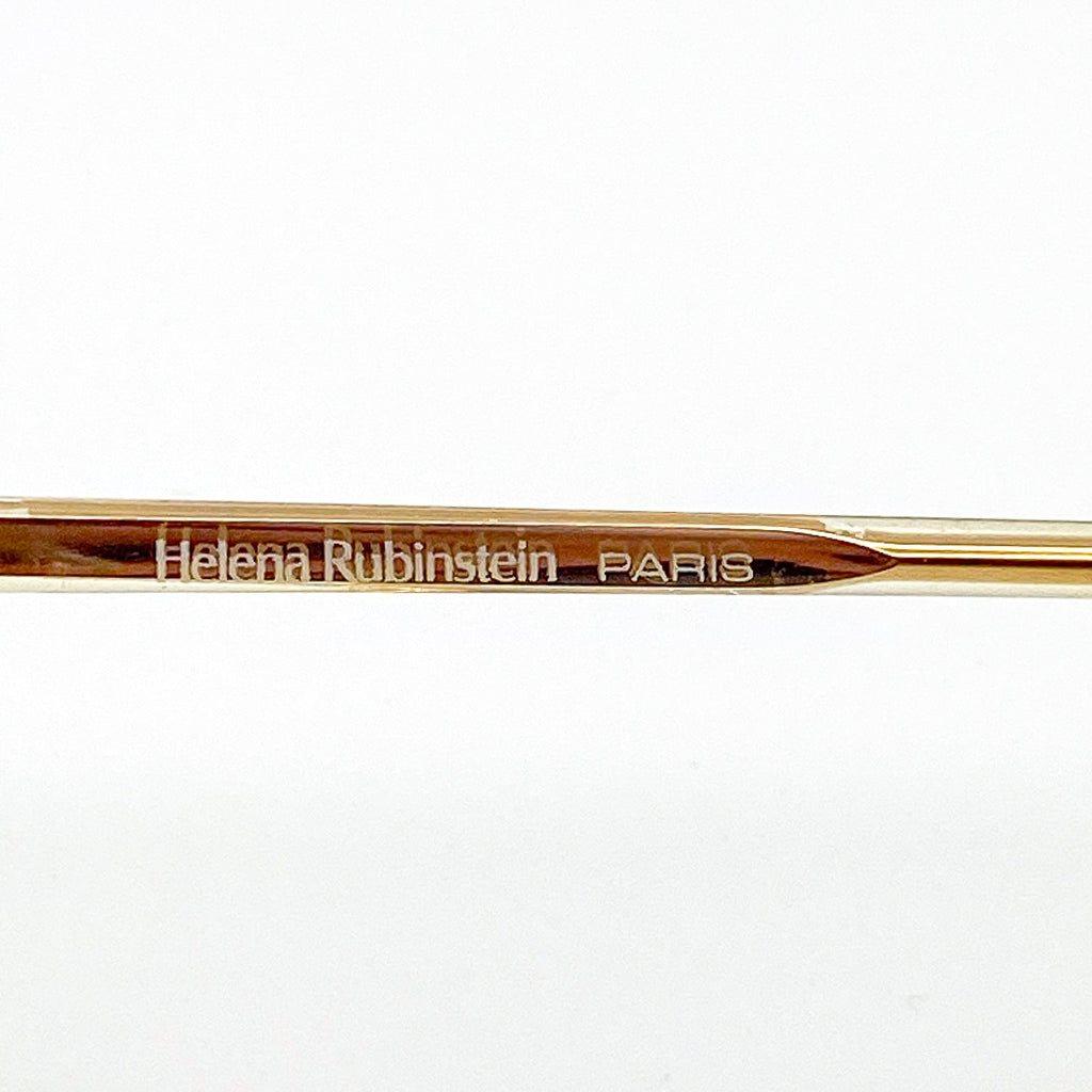 Gold eyeglasses arm with 'Helena Rubinstein Paris' engraving on a white background