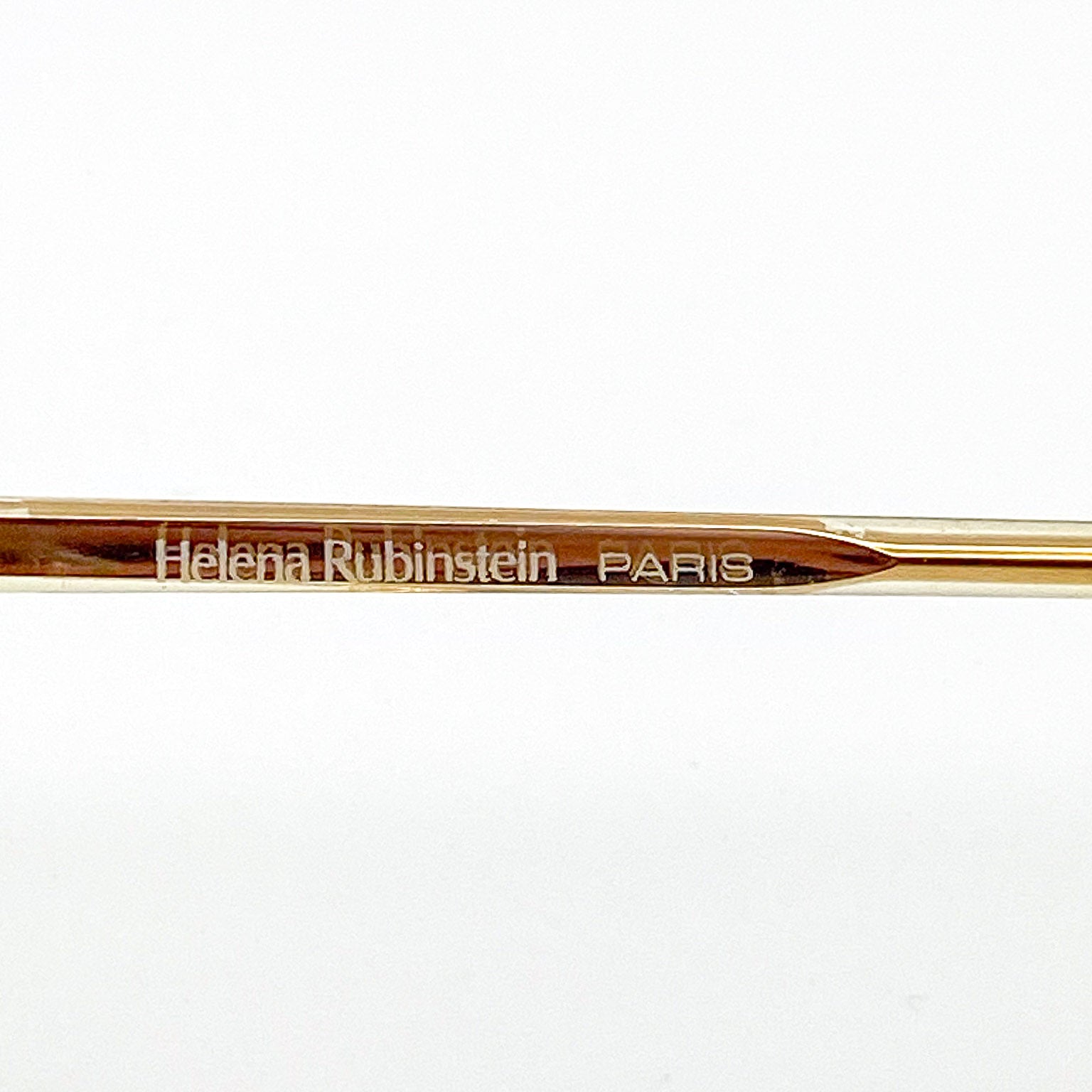 Gold eyeglasses arm with 'Helena Rubinstein Paris' engraving on a white background