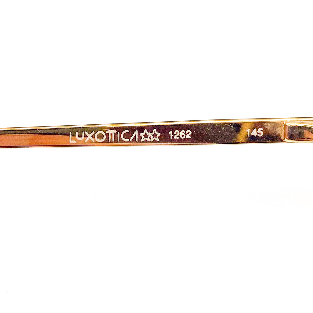 Close-up of a gold eyeglass frame with 'Luxottica' branding on a white background