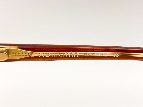 Close-up of a gold-framed eyeglass with 'Luxottica Daphne' on a white background